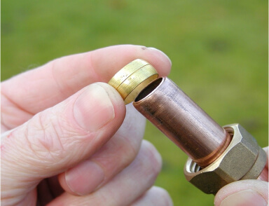 A person holding a brass washer and a copper plumbing fitting, preparing for installation or repair.