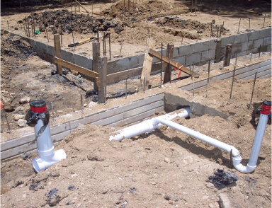 Construction site with exposed plumbing pipes and fittings in sandy soil, ready for installation.