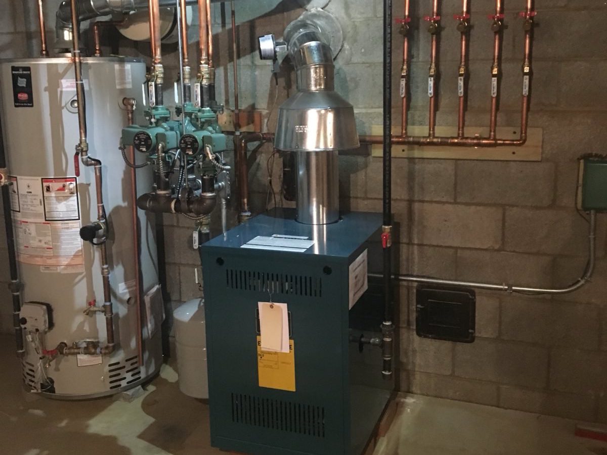 A professionally installed heating system in a basement, featuring a gas boiler, a Bradford White water heater, and an organized copper pipe manifold. Expert plumbing and heating installation for residential systems
